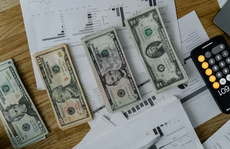 Three U.S. dollar bills on a cluttered desk with papers.